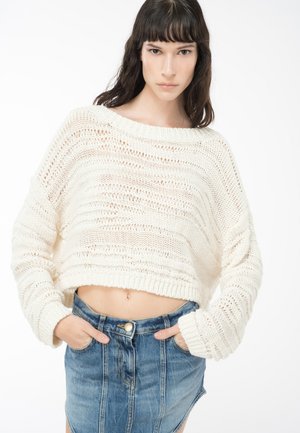 Maglione all'uncinetto color crema con scollatura ampia e maniche lunghe, abbinato a una gonna in denim a vita alta, dotata di tasche frontali e un bottone.