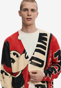 Knit cardigan with red, black, and beige colors; features large cartoon patterns and bold text; button closure, V-neck design.