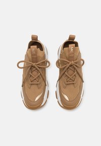 Brown athletic shoes with a mesh upper, textured design, and round white sole. Features laces and a looped heel tab. Gold accents present.