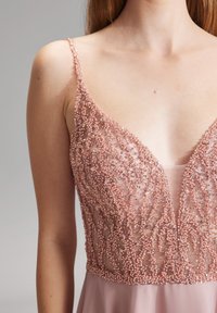 Roze jurk met een subtiele blos, versierd met kralen op het lijfje, met dunne bandjes en een diepe halslijn, van zacht stof dat soepel naar de taille valt.