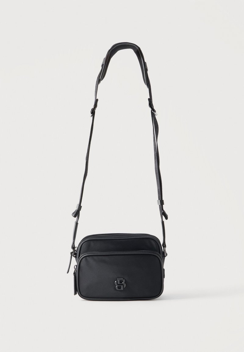 Συμπαγές μαύρο τσαντάκι crossbody με ρυθμιζόμενο λουρί, δύο θήκες με φερμουάρ και ανάγλυφο λογότυπο στην μπροστινή τσέπη.