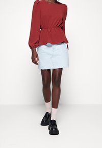 Rød bluse med lange ærmer og indsnævret talje, kombineret med en lyseblå denimnederdel med frynser samt sorte loafers.