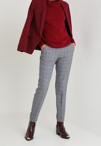 Bordowa marynarka, czerwony golf, szare spodnie w kratę, botki z metalicznymi akcentami. Dopasowany fason, gładka tkanina i czyste linie.