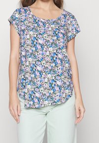 Top a maniche corte floreale con scollatura rotonda. Presenta un mix di fiori rosa, blu e verdi su uno sfondo chiaro. Tessuto morbido.