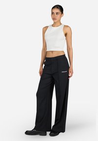White ribbed crop top with a round neckline paired with black wide-leg trousers featuring front pleats and a "PEGADOR" logo accent.