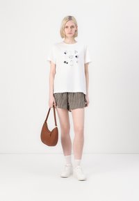Biela bavlnená tričko s grafickými kvetinovými vzormi, spárované s pruhovanými šortkami v hnedých a smotanových odtieňoch. Hnedá crossbody taška a biele tenisky.