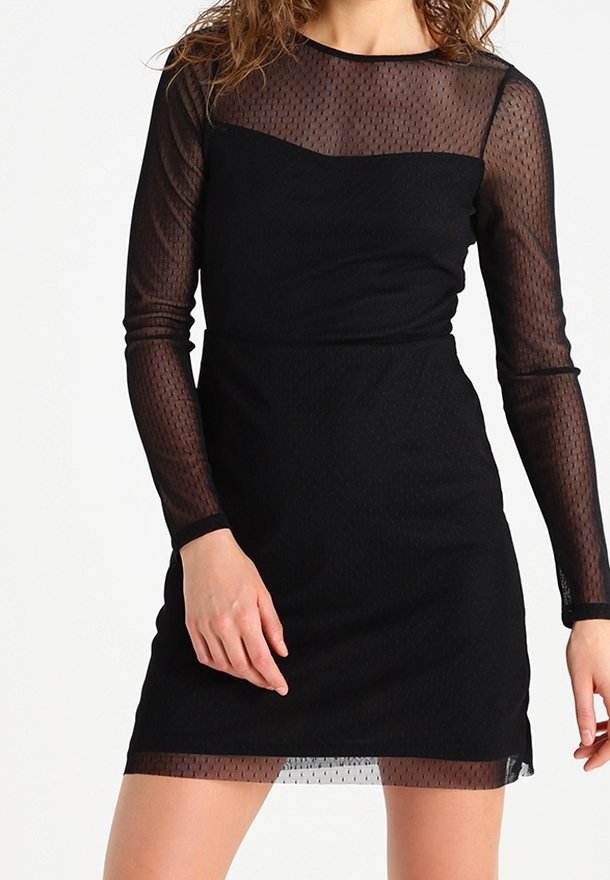 Femme portant une robe noire ajustée avec des manches longues en tulle transparent à pois, détails sur le haut de la poitrine et l'ourlet.
