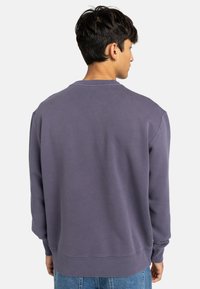 Purple crewneck sweatshirt made of cotton blend, featuring a relaxed fit, ribbed cuffs, and hem, with a smooth texture.