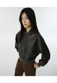 Chaqueta corta de cuero verde oscuro con cuello tipo chaqueta, grandes bolsillos frontales y detalles de costura visibles. Textura suave y corte relajado.
