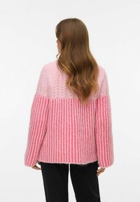 Kootud kampsun, mille alumisel poolel on heleroosa soonikstruktuur ja ülemine osa on ühtlase roosaga, lõdva istuvuse ja pikkade varrukatega.