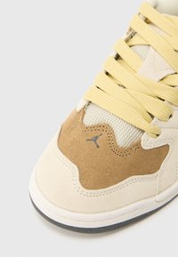 Το αθλητικό παπούτσι διαθέτει επάνω μέρος από μπεζ σουέντ και δίχτυ, κίτρινες κορδόνια και γκρίζο λογότυπο. Καμπύλος σχεδιασμός με ελαστική σόλα και υφασμένους τόνους.