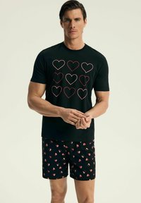 Czarny T-shirt z czerwonymi konturami serc, w połączeniu z czarnymi szortami w różowy wzór serc. Prosta, nowoczesna sylwetka.