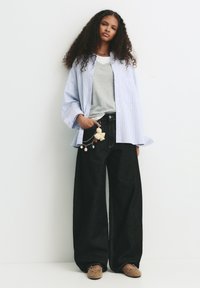 Blå och vit randig oversized skjorta, grå t-shirt, mörka vida jeans och bruna skor med nitar. Nyckelbandstillbehör med olika berlocker.
