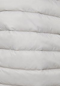 Gros plan d'un tissu matelassé gris clair avec des sections rembourrées horizontales, typique d'une veste ou d'un manteau d'hiver.