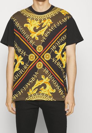 Mężczyzna w czarnej koszulce z krótkim rękawem z brązowym, żółtym i pomarańczowym ozdobnym barokowym nadrukiem oraz wzorami tekstowymi "Versace Jeans Couture".