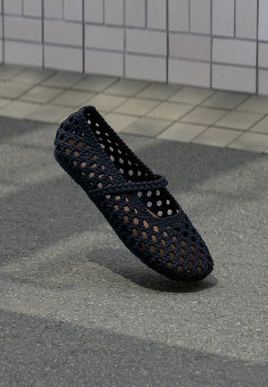 Zwart geweven plat schoen met een ademend, open ontwerp, voorzien van een ronde neus en een decoratieve riem over de bovenkant. Textuur van bovenmateriaal.