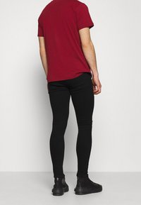 Jeans skinny negros combinados con una camiseta roja. Los jeans tienen una textura suave y un diseño ajustado, complementados por botas negras.
