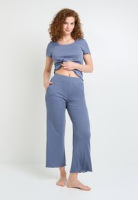 Ensemble de détente en bleu à côtes comprenant un haut à manches courtes avec un col rond et une coupe courte, associé à un bas large, les deux avec un ourlet festonné.