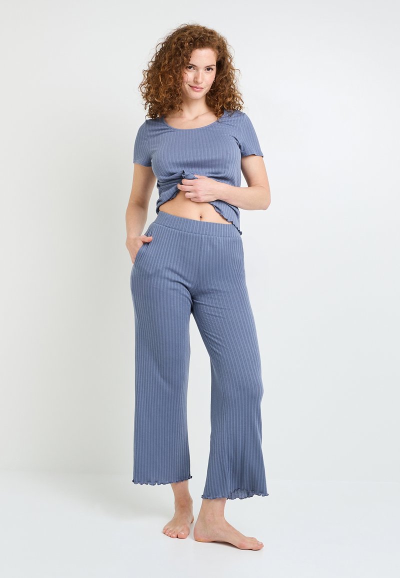 Ensemble de détente en bleu à côtes comprenant un haut à manches courtes avec un col rond et une coupe courte, associé à un bas large, les deux avec un ourlet festonné.