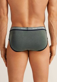 Herrenbrief aus dunkelgrünem Stoff mit glatter Textur. Verfügt über einen weichen Bund mit dem Markennamen und dunkelblauen Akzenten.