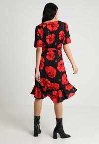 Květinové šaty s motivem červených máků na černém pozadí, krátké rukávy, rozšířený lem a pásek v pase. V kombinaci s černými kotníkovými botami.