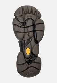 Sole di scarpa Vibram nera e grigia con superficie texture, motivo di battistrada unico e logo Vibram giallo in evidenza.