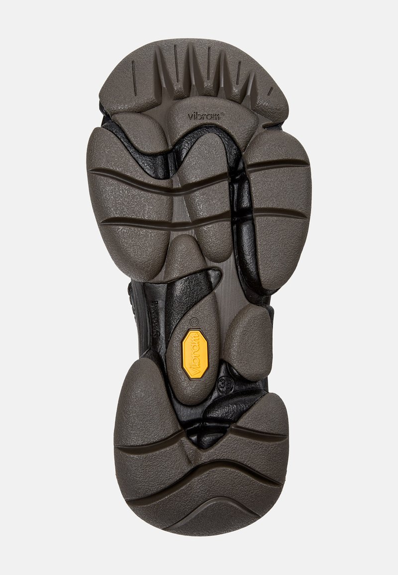 Sole di scarpa Vibram nera e grigia con superficie texture, motivo di battistrada unico e logo Vibram giallo in evidenza.