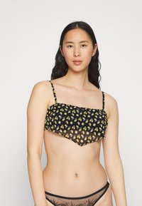 Top de biquíni preto com padrão floral amarelo. Borda inferior transparente com corte triangular. Alças finas e ajustáveis acentuam o design.