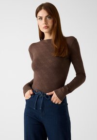 Bruine top met lange mouwen en een getextureerd diamantpatroon, gecombineerd met donkerblauwe high-waisted jeans met een taillekoortje.