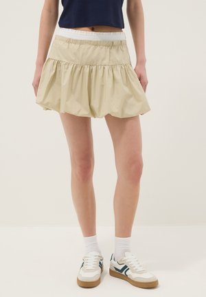 Persona que lleva una minifalda beige con vuelos, zapatillas blancas con detalles azules, calcetines blancos y un top corto azul marino.