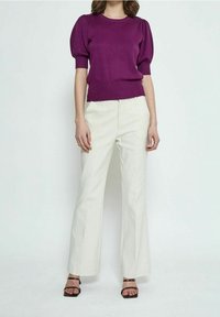 Lila gestricktes T-Shirt mit kurzen Puffärmeln, kombiniert mit weißen weit geschnittenen Hosen und schwarzen Sandalen mit Absätzen. Glatte Stoffqualität, taillierter Schnitt.