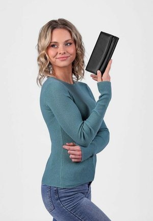Černá kožená peněženka držená osobou v proužkovaném smaragdově modrém svetru a modrých džínách, která se vyznačuje hladkou texturou a strukturovaným designem.