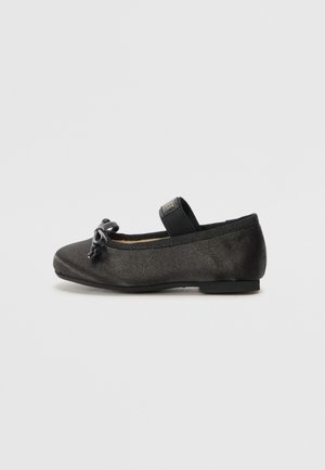 Black flat shoe made of soft fabric, featuring a round toe, a bow accent, and an elastic strap for secure fit. Low, flat sole.