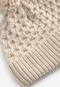 Berretto lavorato a maglia in morbido filato beige, con un motivo testurizzato e un pompon rotondo sulla parte superiore. Fascia a coste nella parte inferiore per una vestibilità aderente.