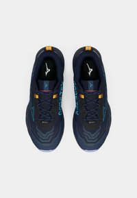 Modré a čierne bežecké topánky so štruktúrovanými prekrytiami, značkou Gore-Tex a kontrastnými žltými detailmi. Dajú sa šnurovať a majú gumovú podrážku.