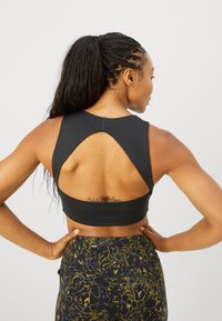 Sujetador deportivo negro con diseño de espalda de nadador y detalle recortado. Tejido suave con un acabado mate. Banda elástica con logotipo en la parte inferior.