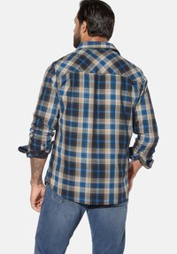 Karierte Hemd in Blau-, Braun- und Beigetönen. Mit langen Ärmeln, spitzem Kragen und abgerundetem Saum. Material wirkt gewebt.