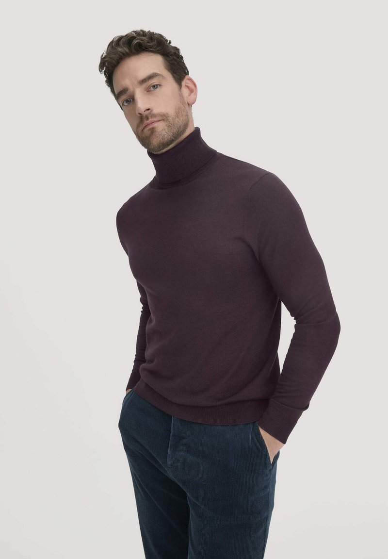 Dunkellila Rollkragenpullover aus einem weichen, texturierten Stoff. Hat lange Ärmel und eine figurbetonte Passform. Kombiniert mit dunkelblauen Kordsamt-Hosen.