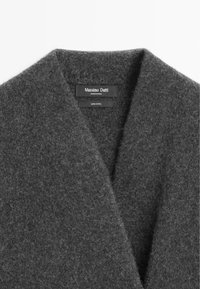 Cardigan in lana grigia con collo scialle, texture morbida e un'etichetta con la scritta "Massimo Dutti," che indica una composizione 100% lana.