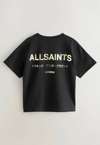 Melna kokvilnas T-kreklu īsām piedurknēm ar zeltā drukātu tekstu "ALLSAINTS" un "LONDON", ar japāņu rakstzīmēm apakšā.