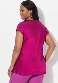Haut fuchsia à manches courtes avec une coupe décontractée, texture lisse et fentes sur les côtés au niveau de l'ourlet, associé à un pantalon violet.
