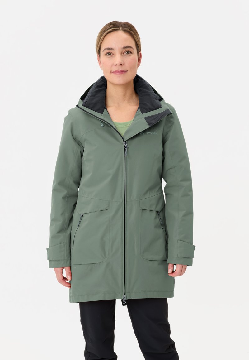 Groene waterdichte jas met een zwarte capuchon, frontrits, twee grote zakken en een relaxed fit. Materiaal lijkt glad en duurzaam.