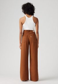 Kankkurot mustat housut teksturoidussa kankaassa, korkealla vyötäröllä ja kahdella takataskulla. Asu on viimeistelty istuvalla valkoisella toppilla.