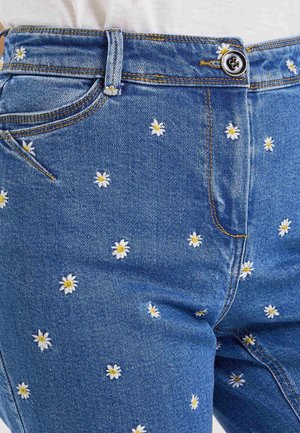 Pantalones vaqueros azul denim con pequeñas margaritas blancas y amarillas bordadas repartidas por la tela, con botón y presilla para cinturón.