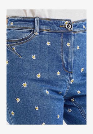Pantalones vaqueros azul denim con pequeñas margaritas blancas y amarillas bordadas repartidas por la tela, con botón y presilla para cinturón.