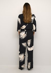 Combinaison noire avec motif de feuilles blanches, présentant une coupe décontractée, des manches trois-quarts et une taille cintrée. Tissu doux avec une texture lisse.