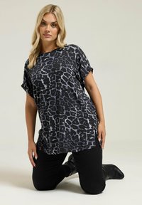 Top negro con estampado de leopardo, de manga corta, con cuello redondo y aberturas laterales, combinado con pantalones negros ajustados y botas negras hasta la rodilla.