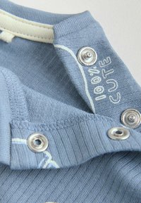 Tela azul claro de canalé con botones de presión de metal y texto impreso en blanco que dice "love CUTE" en un cuello o puño doblado.