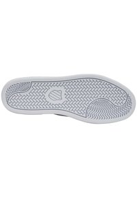 Sole of a sneaker in white rubber with a textured herringbone pattern. Features a shield logo at the center and smooth edges for grip.
