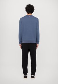 Sudadera azul de cuello redondo con puños acanalados, combinada con pantalones de chándal negros con bolsillos laterales. Zapatillas blancas con acentos negros.